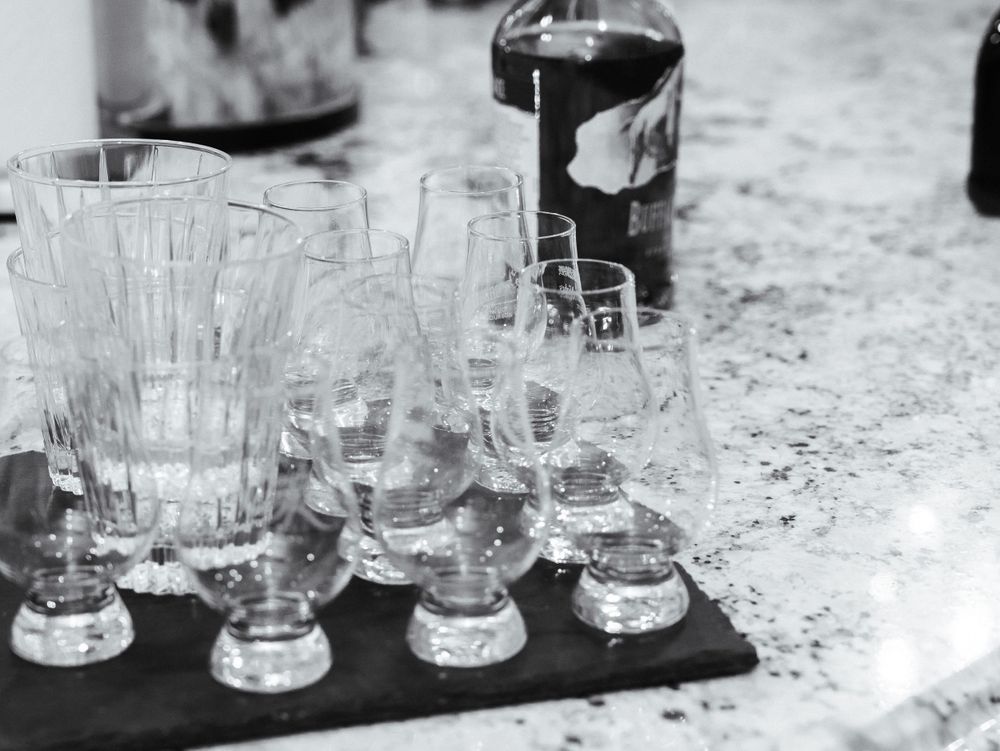 Black and white photo of empty cocktail glasses arranged on a serving tray with a dark bottle in the background.