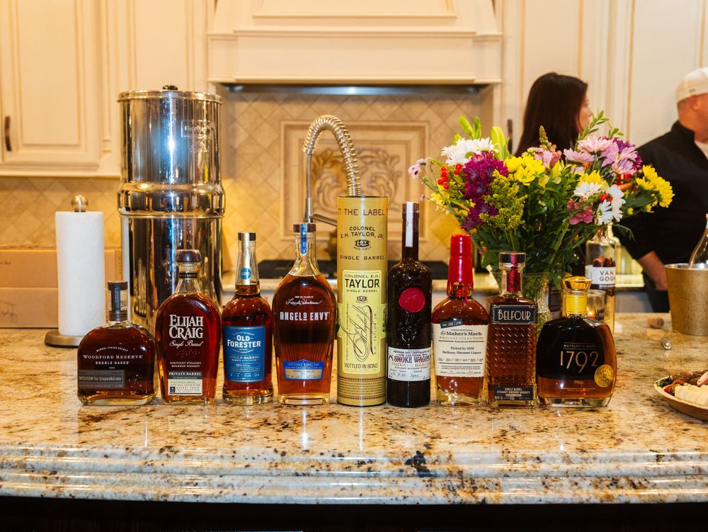 Various liquor bottles and spirits displayed on a granite countertop with fresh flowers in a vase as decoration.