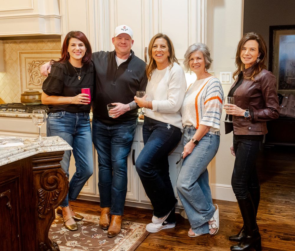 A group of friends in casual jeans and tops gather together for a photo in an elegant room with ornate wood decor.