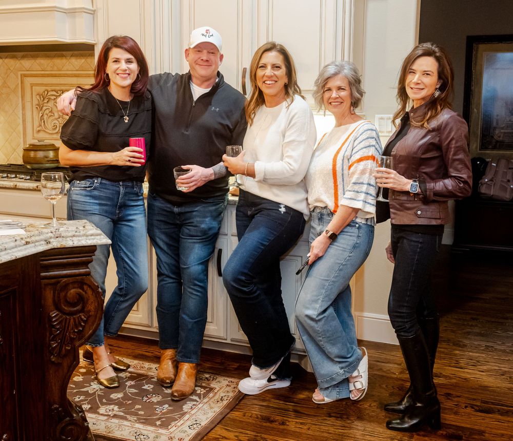 A group of five people in casual attire standing together and smiling in a rustic kitchen setting.