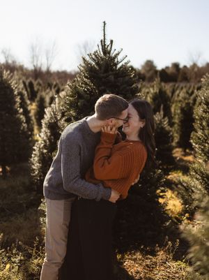 A romantic embrace among Christmas trees at sunset.