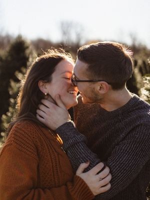 A romantic couple in sweaters share an intimate moment among evergreen trees at sunset.