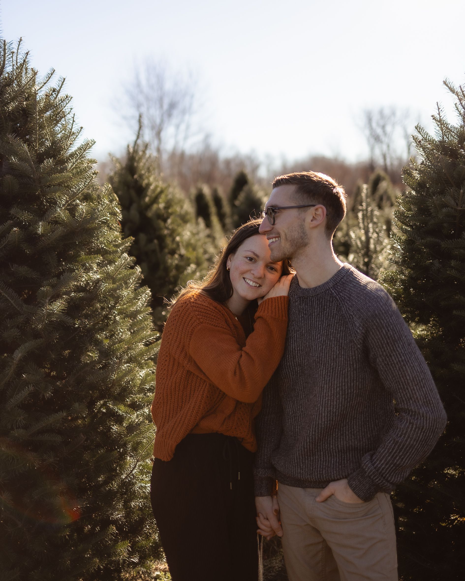 Couple in cozy sweaters sharing a tender moment among evergreen trees.