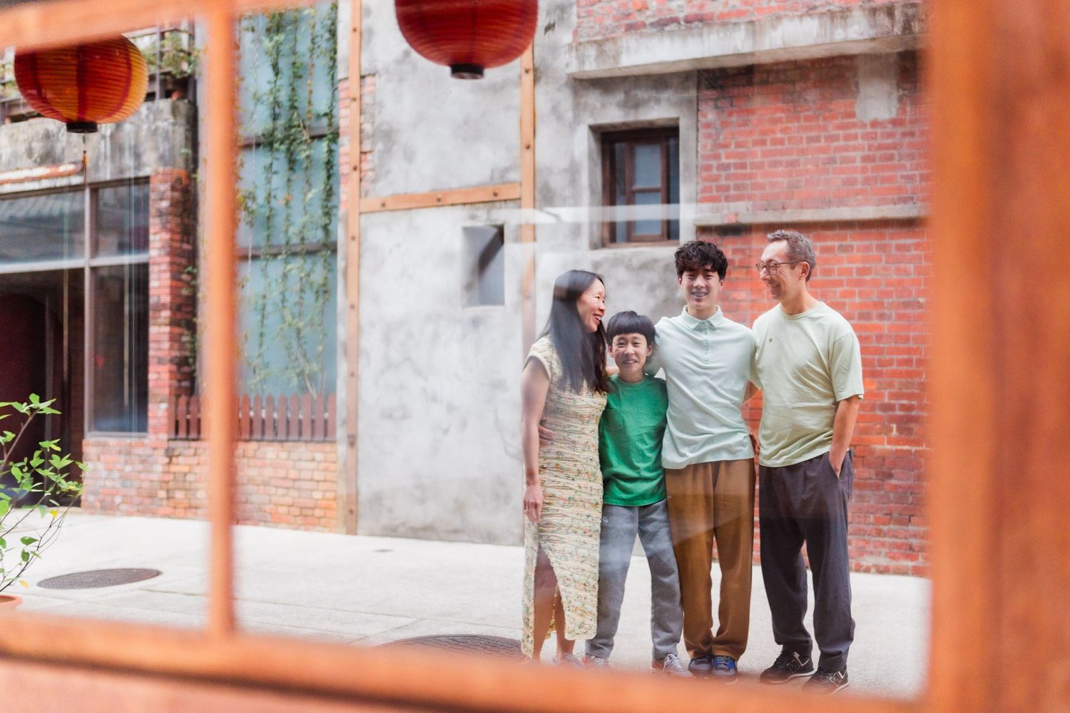 A family poses together in an urban setting with red lanterns and brick buildings at Bopiliao Historical Block in Taiwan.