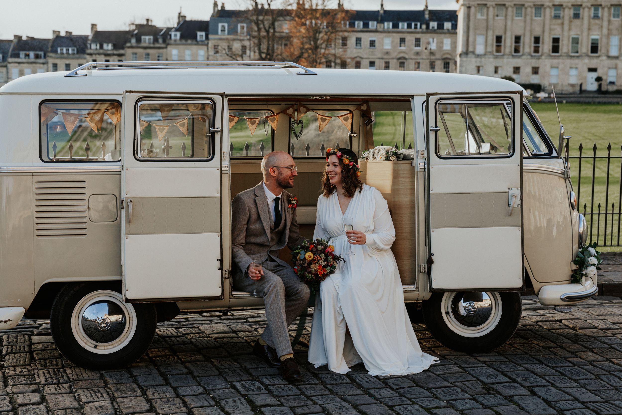 Bride and groom posing by a vintage campervan at the Royal Crescent in Bath during golden hour.