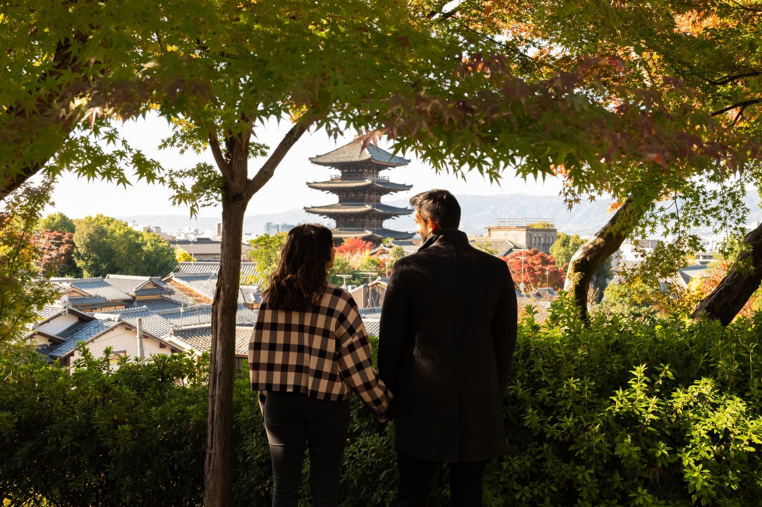 Couple admiring a stunning view of a five-story pagoda through lush autumn foliage in Kyoto.