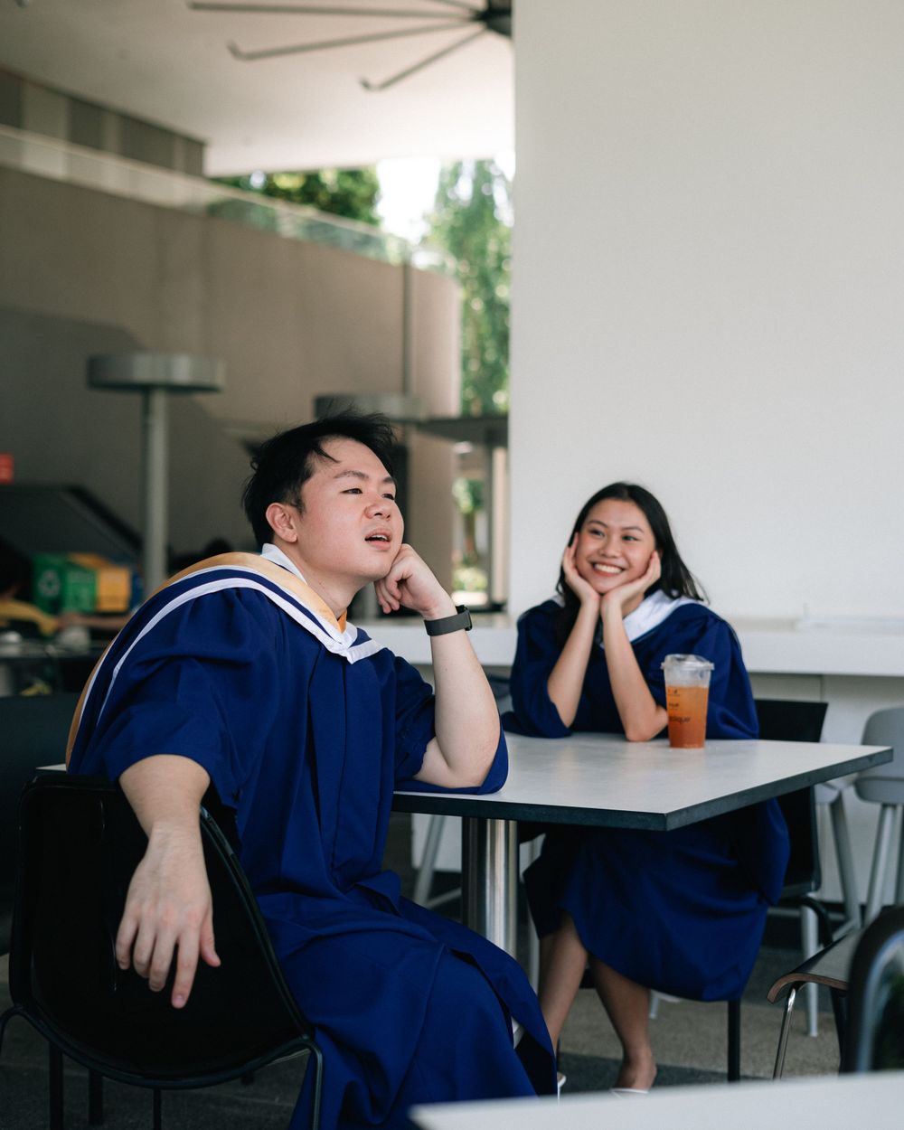 Students in graduation attire sharing a lighthearted moment at a table.