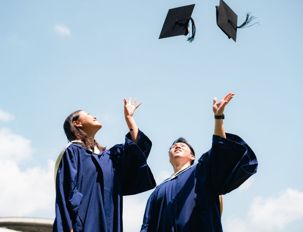 Graduates tossing mortarboards into a bright blue sky during celebration.