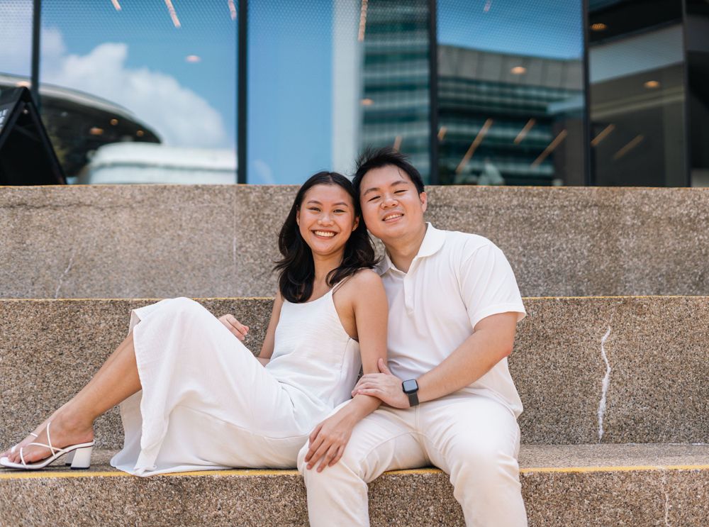 Couple in white outfits sitting on stone steps for an engagement photo.