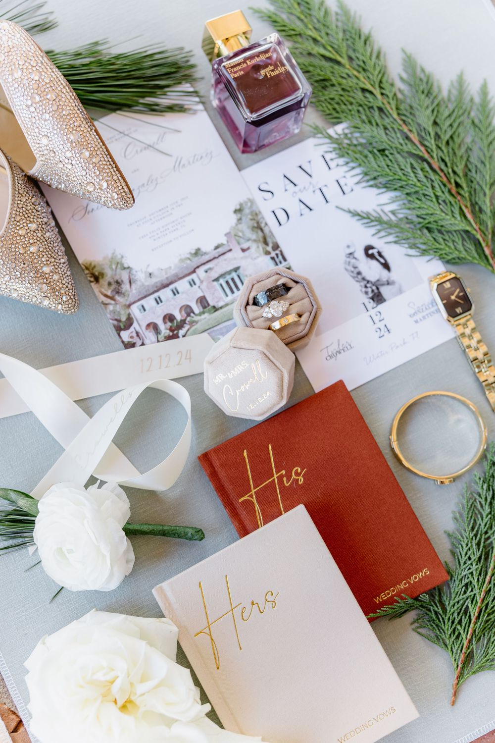Elegant wedding stationery flatlay with white and burgundy cards, evergreen sprigs, and gold accents on marble surface.
