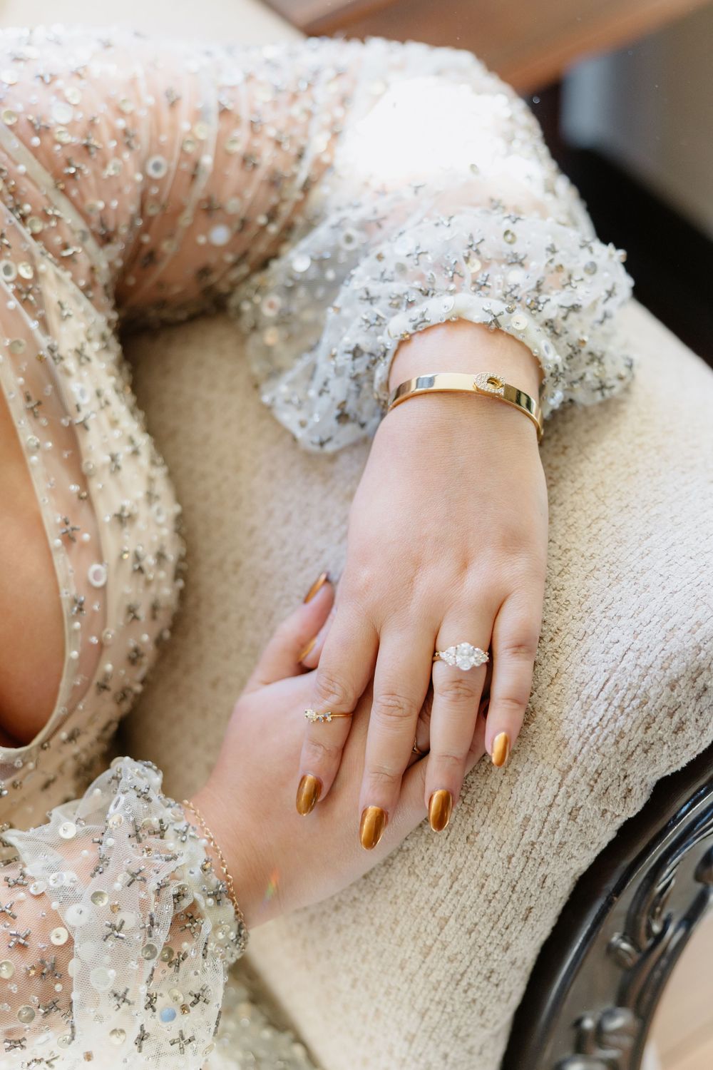 Close-up of hands wearing a delicate beaded dress against a light textured background.
