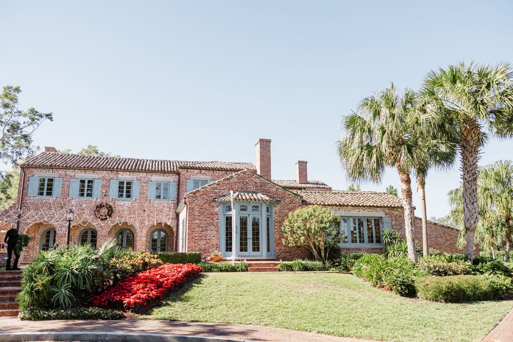 Mediterranean style mansion with pink stucco exterior, palm trees, and vibrant red flowers in the landscaping.