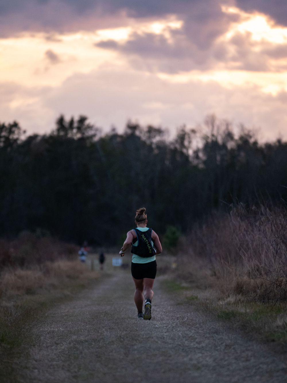 Silhouette of runner on trail path during sunset with dramatic cloudy sky.