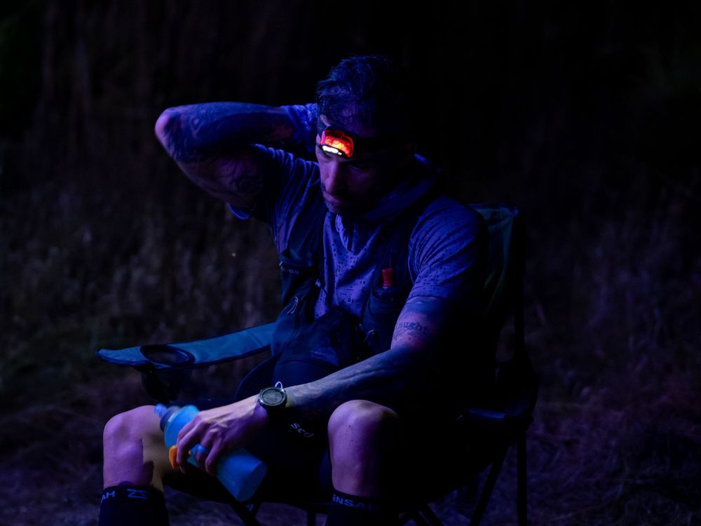 Runner resting in chair at night wearing headlamp during endurance event.