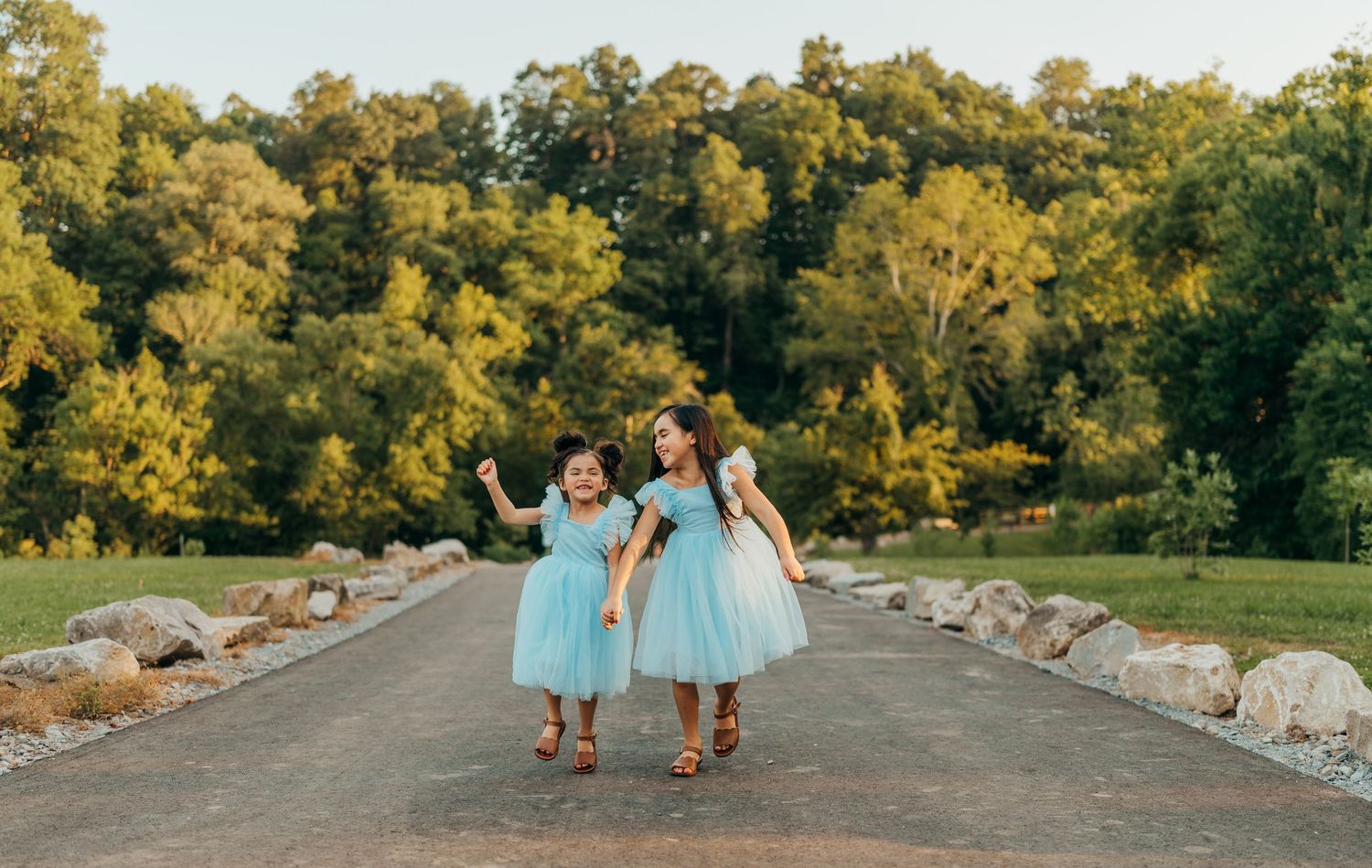 Friends in matching blue dresses walking together on tree-lined path at sunset. Clarksville Tn photographer