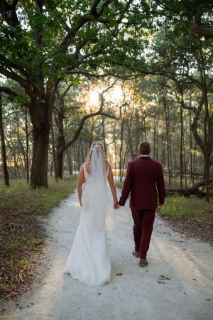 A sunset wedding photo shows a couple walking hand in hand down a forest path.