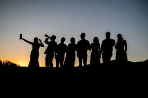 Group silhouette of people standing on a hill during sunset taking selfies.