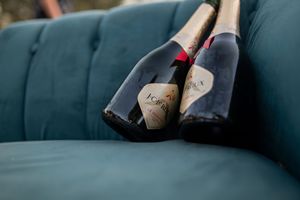 Two champagne bottles with custom labels resting on a teal velvet couch.