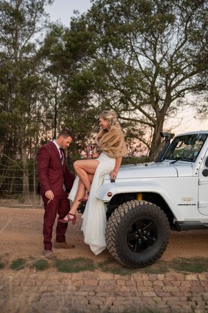 Wedding couple posing with a white Jeep on a rustic brick road at sunset.