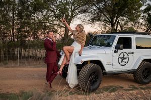 Newlyweds sharing a playful moment by a white Jeep during golden hour.
