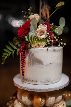 Semi-naked wedding cake adorned with burgundy and blush roses and eucalyptus.