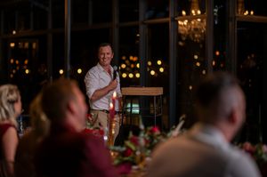 Wedding guest delivering speech at reception with warm lighting and floral decorations.