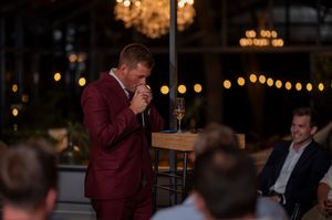 Wedding guest in burgundy suit giving speech during evening reception.