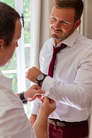 Sequence of formal preparation shots showing details of white shirts and burgundy ties.