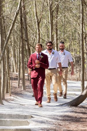 Wedding party walking along a sunlit forest path in formal attire.