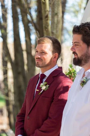 Two members of a wedding party stand together during an outdoor ceremony in the woods.