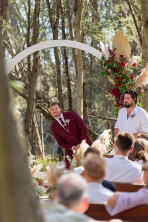 Joyful moment during an outdoor forest wedding ceremony under a decorated white arch.