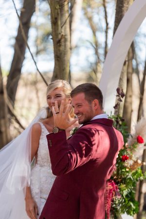 Emotional wedding moment captured under floral arch in forest setting.