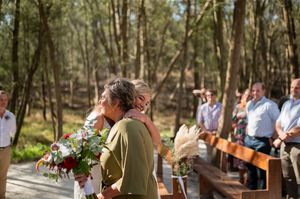 A modern outdoor forest wedding ceremony setting with a white arch and burgundy floral decorations.