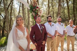 Warm sunlight filters through trees at an outdoor wedding venue with rows of wooden benches.