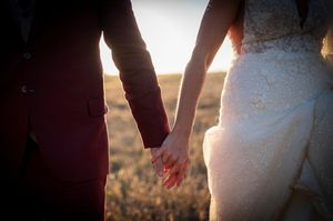 Artistic silhouette of bride and groom holding hands at sunset.