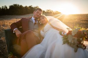 Romantic sunset portrait of newlyweds relaxing in a field during golden hour.
