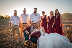 Wedding party in burgundy and neutral attire poses together at sunset in field.
