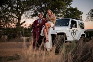 Couple poses with white Jeep during sunset wedding photoshoot.