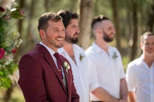 Wedding party standing together outdoors with groomsmen in white and burgundy attire.