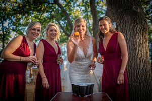 Wedding party in burgundy dresses gathered around bride for candid outdoor photos.