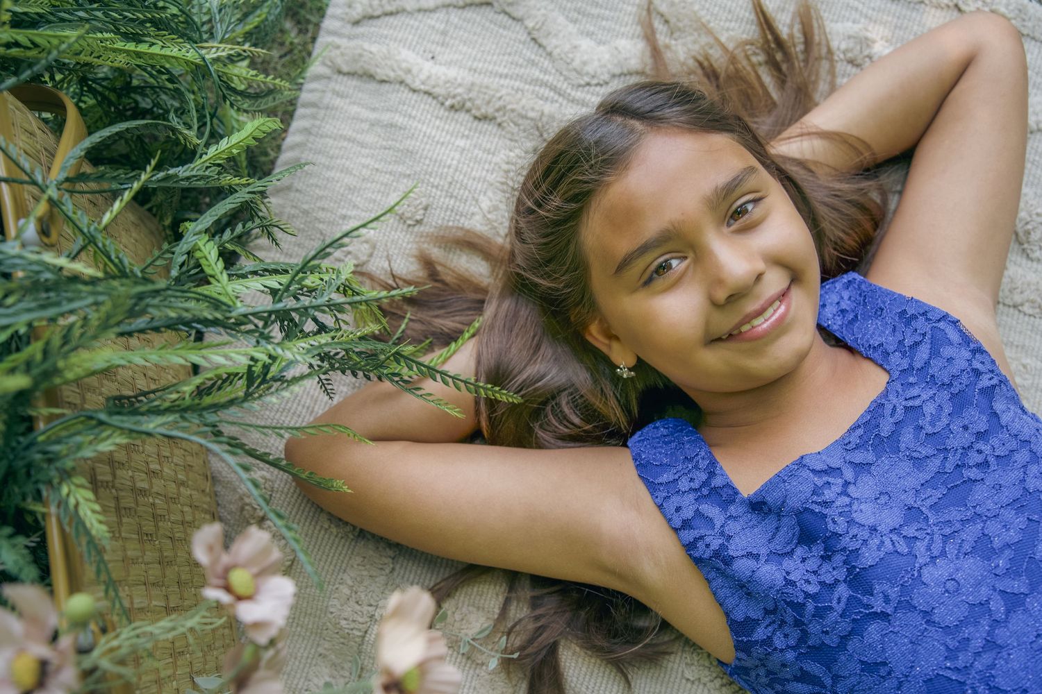 Person in blue floral lace top lying on weathered wooden deck surrounded by plants and greenery.