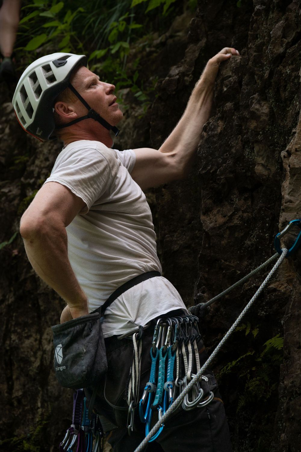 Rock climber ascending steep wall with climbing gear and chalk bag visible.
