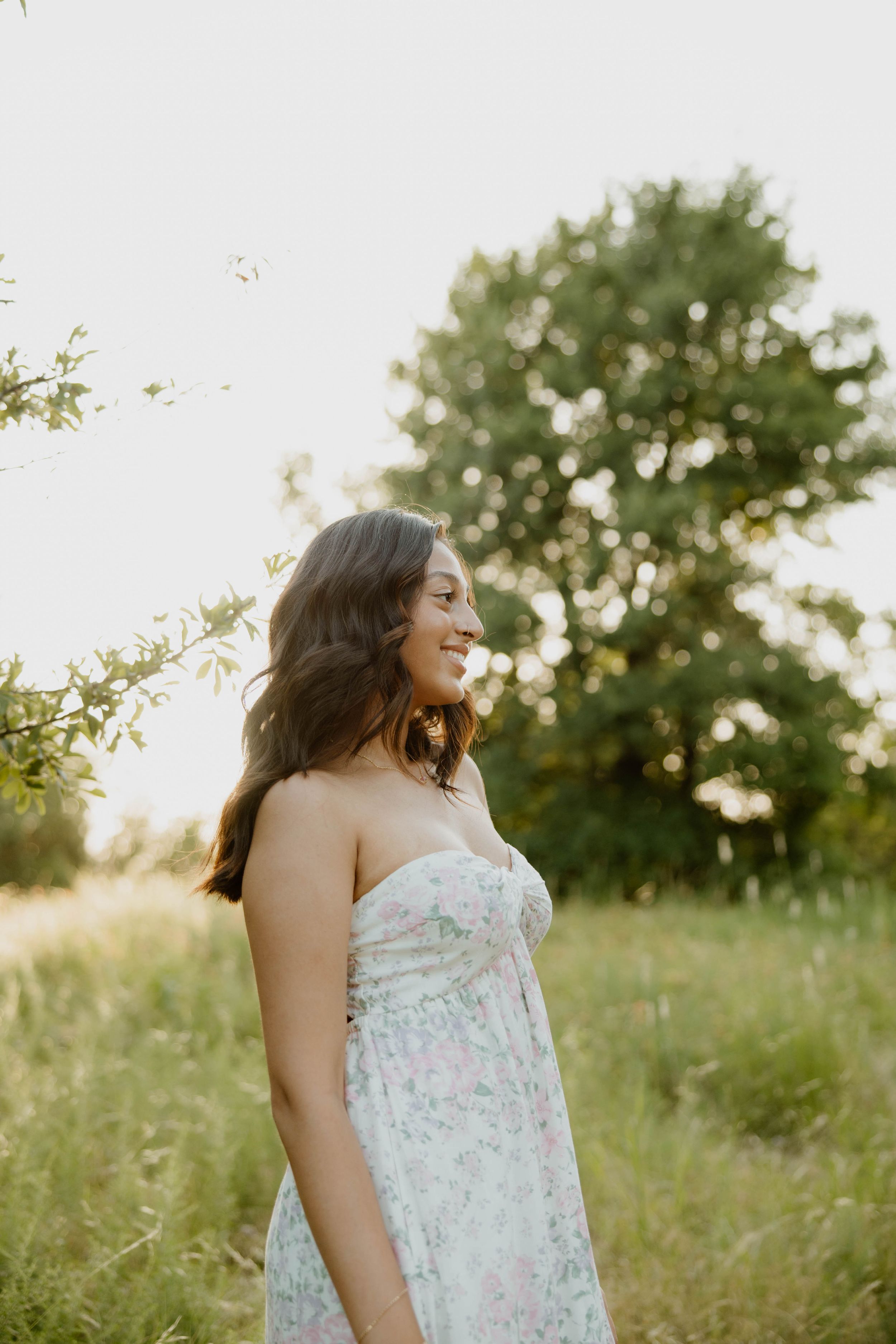 A floral white dress is illuminated by soft sunlight in a rustic meadow setting.