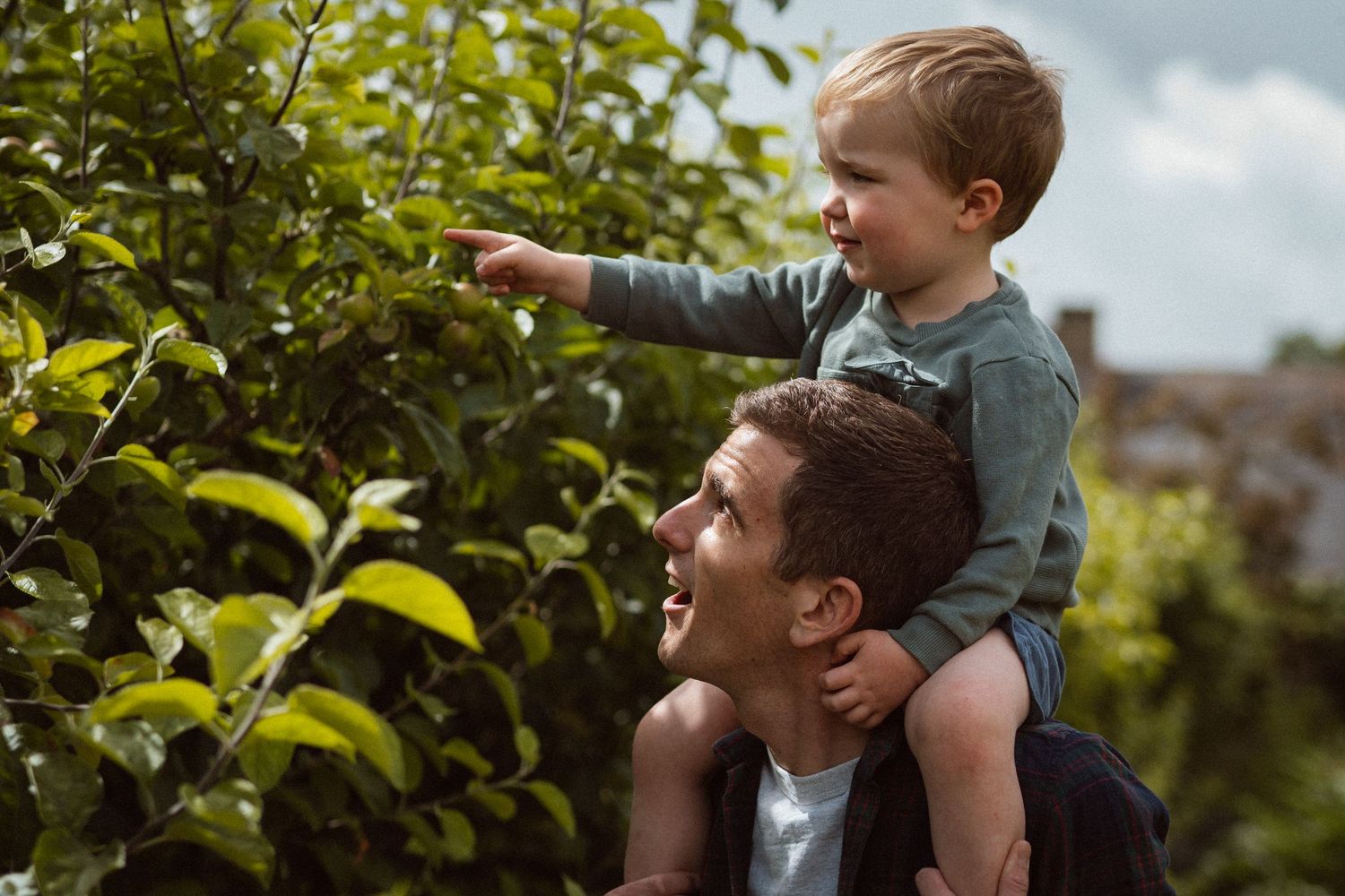 A joyful pair outdoors among green foliage as one carries the other on shoulders in a garden setting.