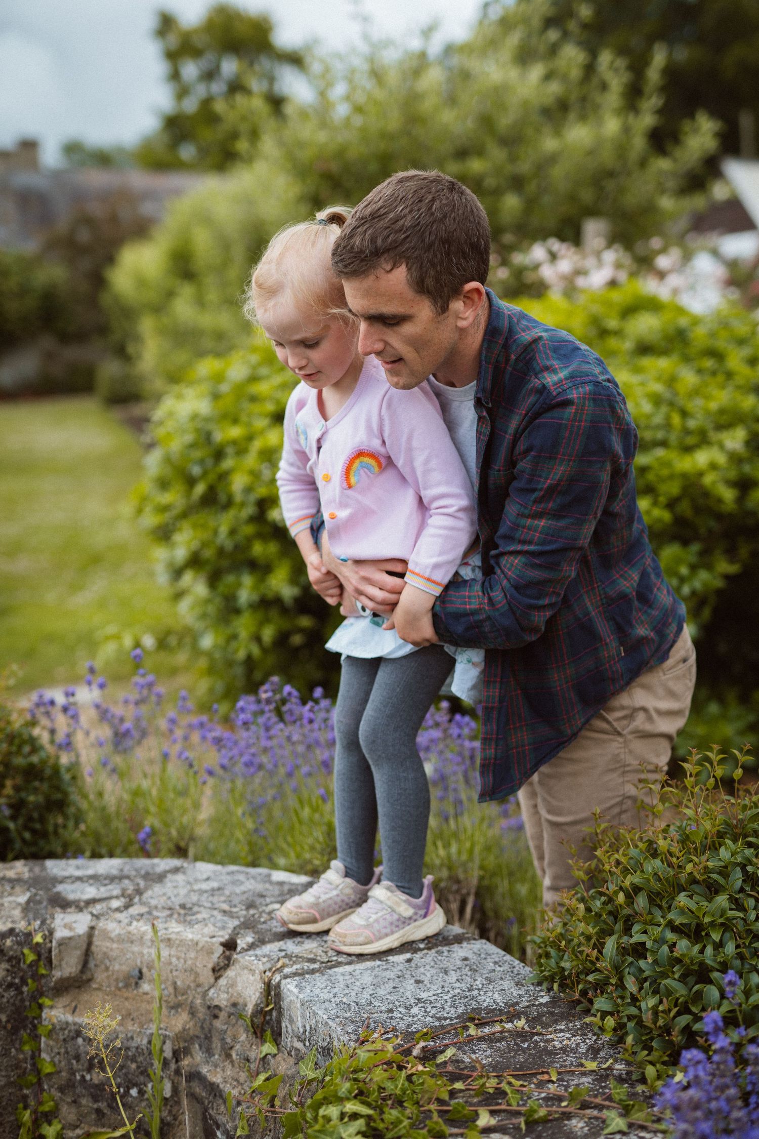 Two people share a joyful moment in a garden with purple wildflowers and lush greenery.