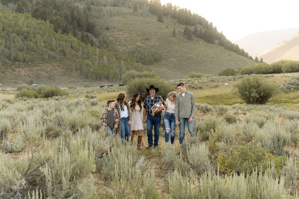 Family group walking together through sagebrush along a mountain trail at sunset.
