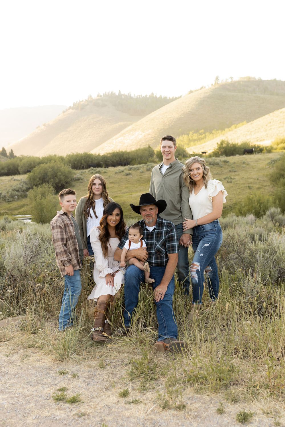 Extended family group portrait in casual western wear against rolling hills at sunset.
