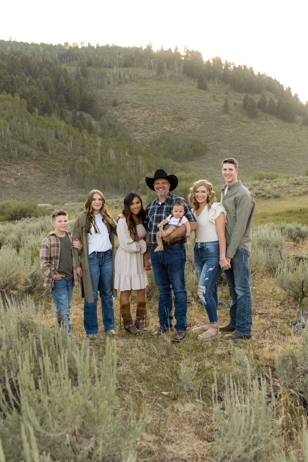 Extended family posing together on mountain hillside with sagebrush at sunset.