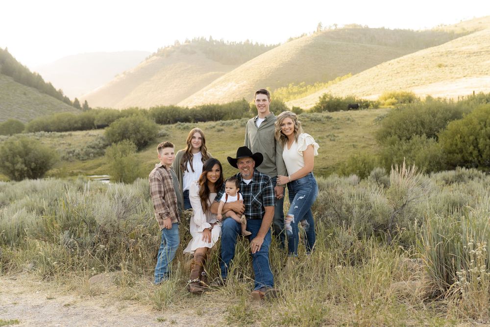 Group of people gathered together outdoors in a rustic mountain setting with sagebrush and golden hills at sunset.