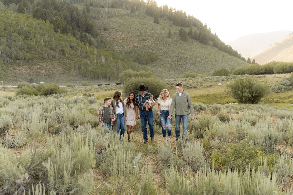 Group of people walking together through sage brush on mountain trail at sunset.